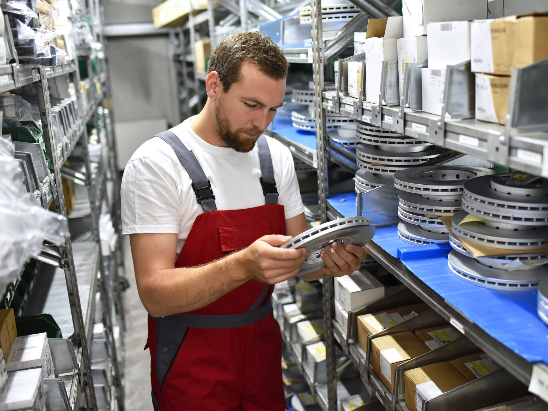 Automechaniker im Warenlager mit Ersatzteilen - Fahrzeugreparatur Bremsscheiben // Car mechanic in the warehouse with spare parts - Vehicle repair brake discs